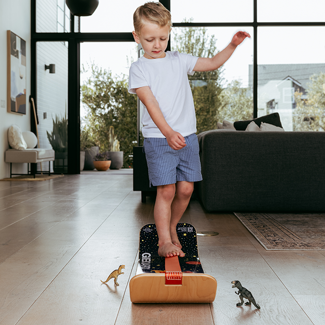 Child playing with an astro skackboard on a wooden floor in a living room.