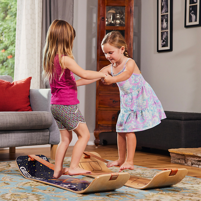 Two young girls playing on slackboards in a living room.