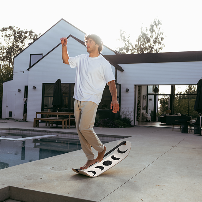 Person riding a moon slackboard on a patio with a modern house in the background