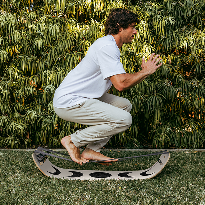 Man balancing on a moon slackboard plus outdoors with greenery in the background